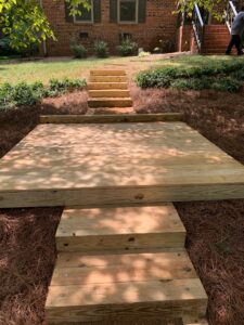 A small wood deck with wooden stairs on two sides. Fresh pinestraw completes the project.