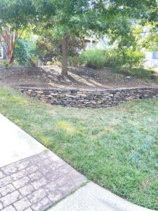 A stone retaining wall seperating a mulched planting area and a lawn